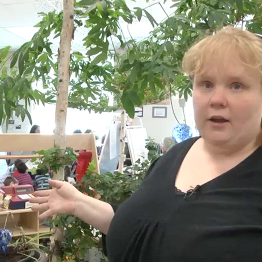 Teacher Shara-Lynn talking to camera with indoor tree in background